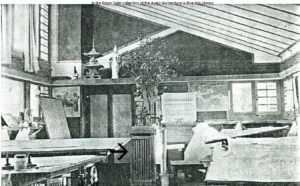 Photograph ahosing Taliesin drafting studio with drafting tables, Asian art, and models. An arrow points at a radiator cover in the studio.