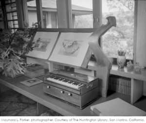 Black and white photograph looking at built-in bookcase at wall in Frank Lloyd Wright's bedroom. Includes an oar lock, a harmonium, and a special box for holding Wright's architecture medals.