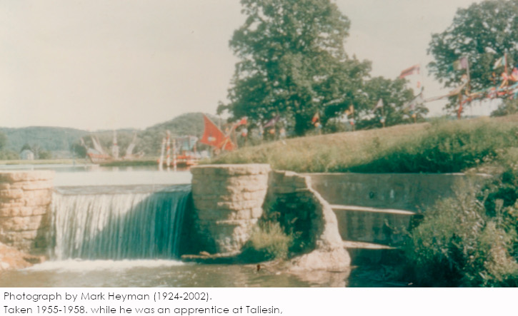 Color photograph by Mark Heyman. Shows waterfall, stonework, and people with flags in distance.