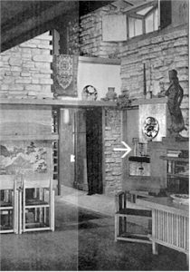 Black and white photograph looking southwest in Taliesin Living Room, 1937. In view: wooden chairs and funiture, light limestone walls. Photograph has an arrow pointing at a wooden door.