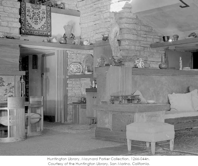 Black and white photograph looking southwest in Taliesin's living room. Taken by Maynard Parker in 1955. In view: wooden furniture, plaster on walls, artifacts on tables.